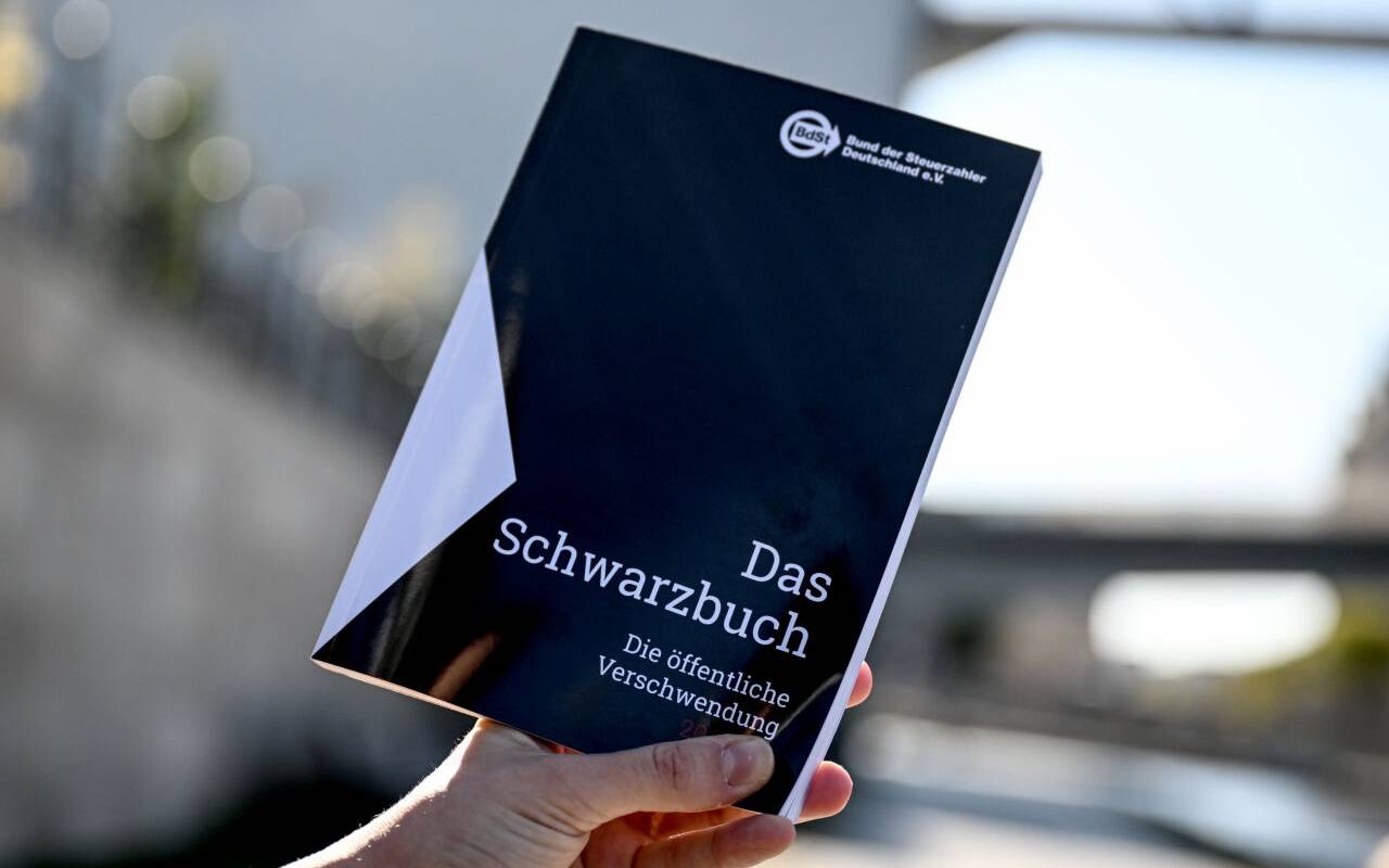Das Schwarzbuch 2025/26 vom Bund der Steuerzahler in wird vor das Reichstagsgebäude gehalten. Das Schwarzbuch listet Beispiele auf, wo aus Sicht des Steuerzahlerbunds Steuergelder verschwendet wurden.