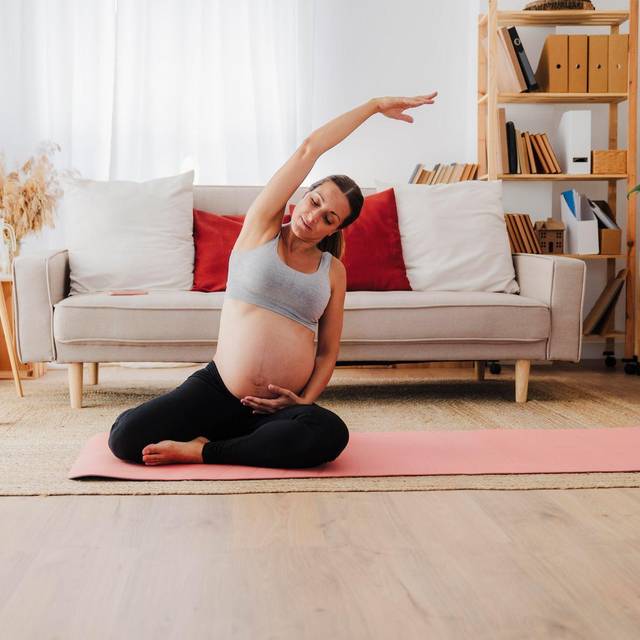 Eine Schwangere macht Dehnübungen auf einer Yogamatte
