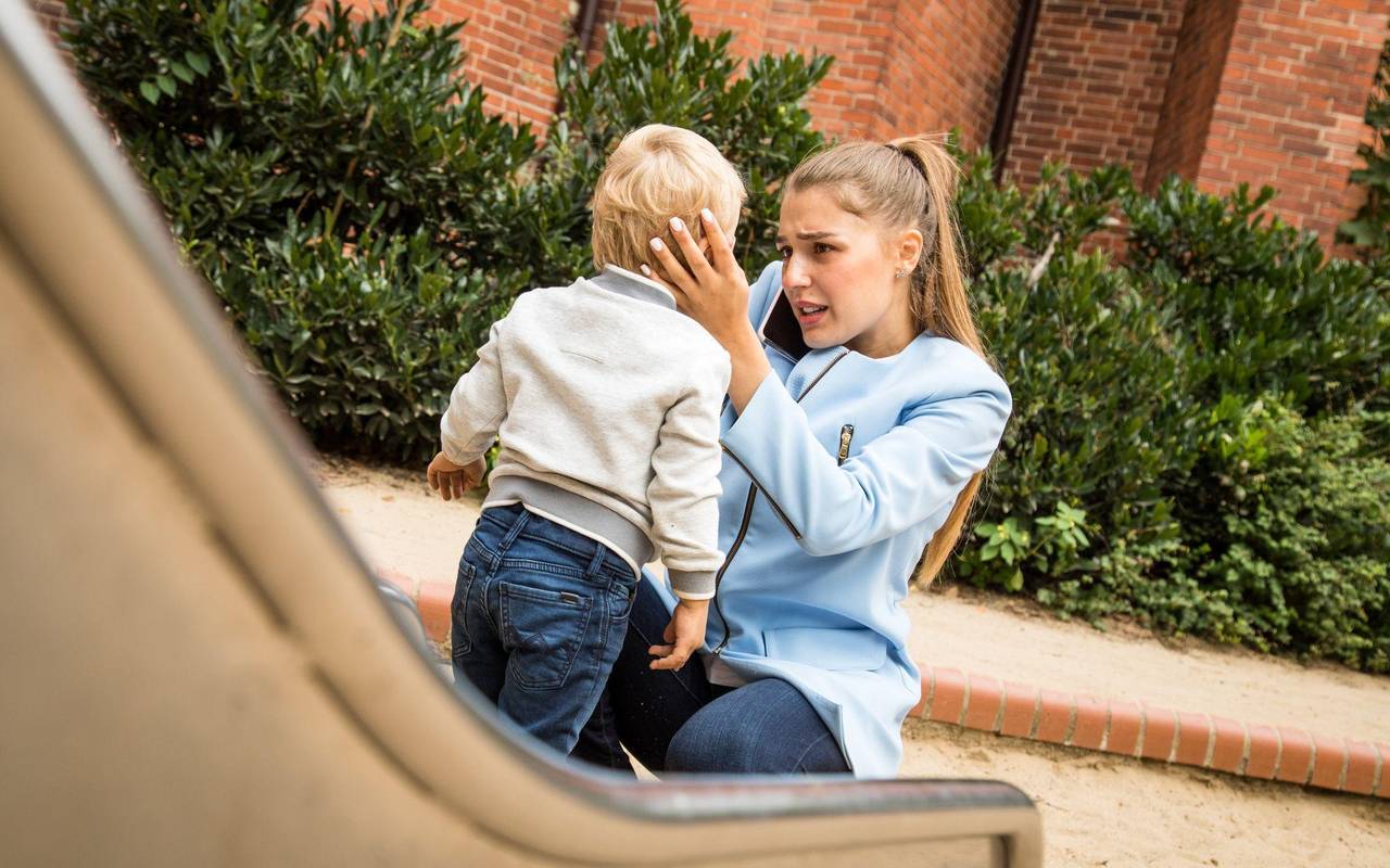 Mutter hält auf dem Spielplatz besorgt den Kopf ihres Kindes