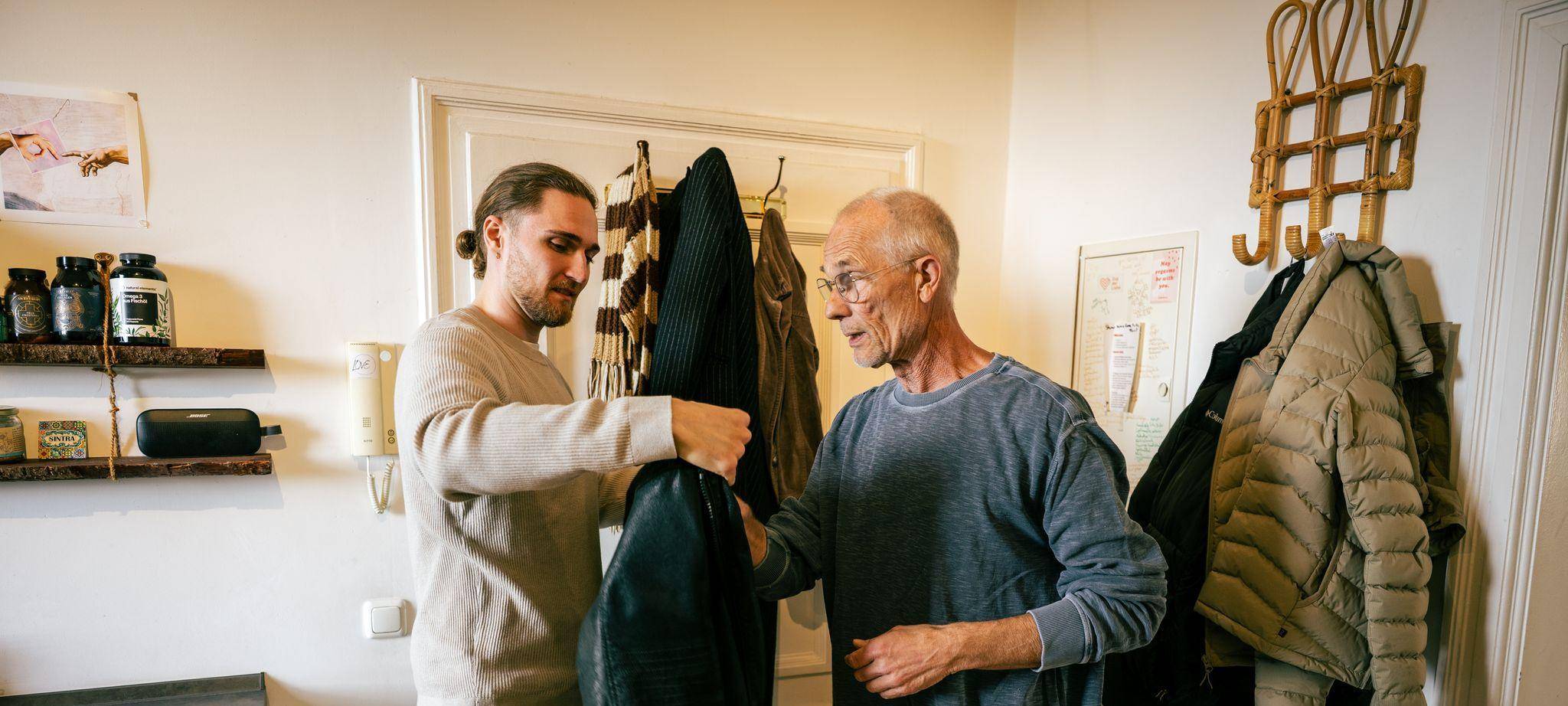 Ein junger Mann hilft einem Senior die Jacke anzuziehen