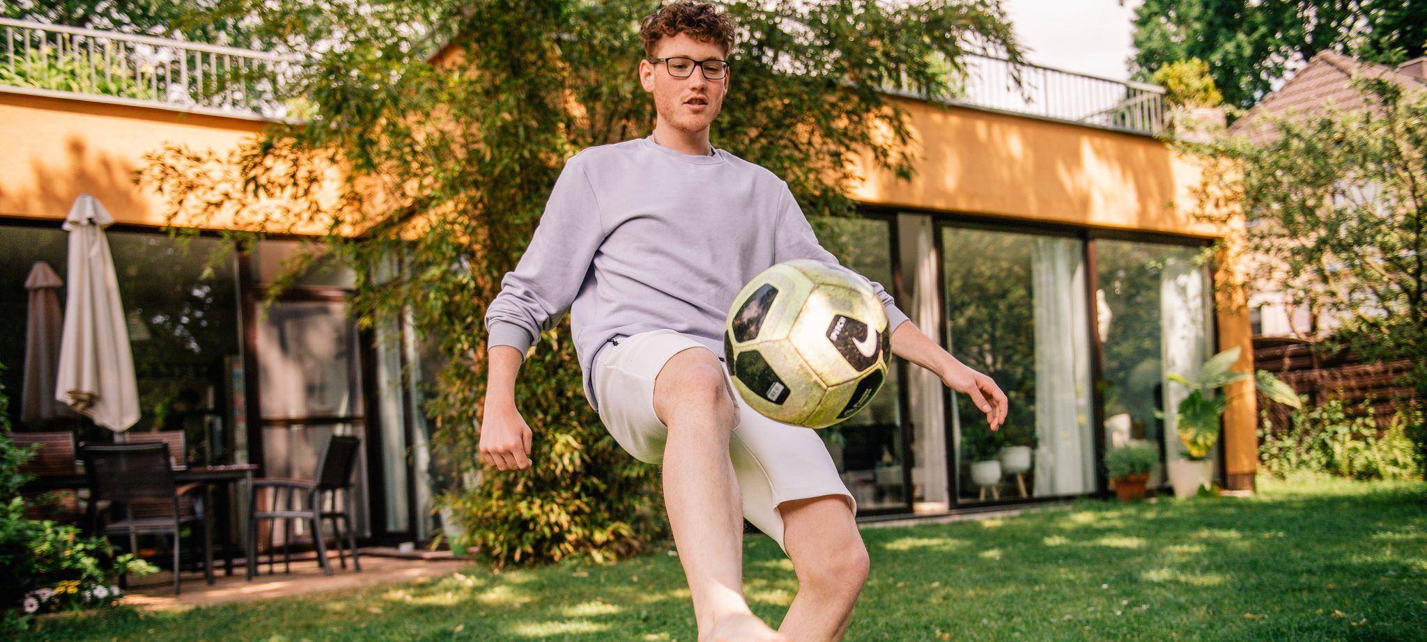 Junger Mann kickt einen Fussball barfüßig im Garten