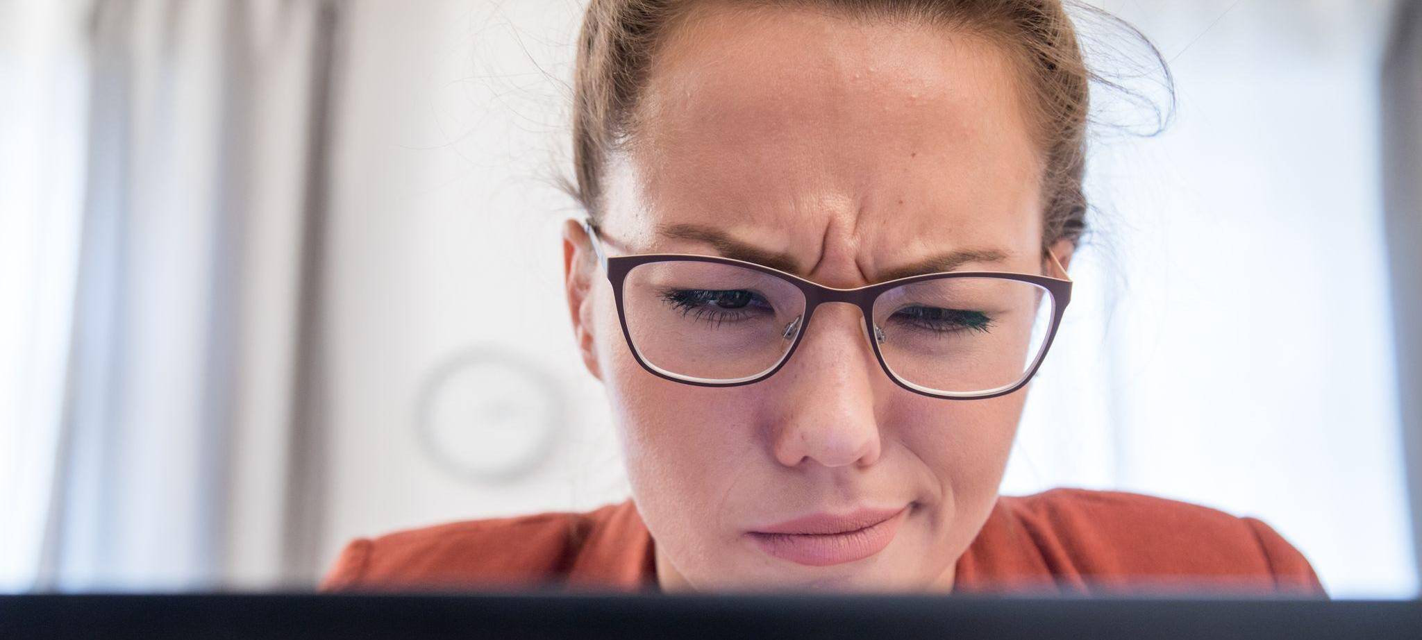 Eine Frau verzieht das Gesicht vor einem Laptop