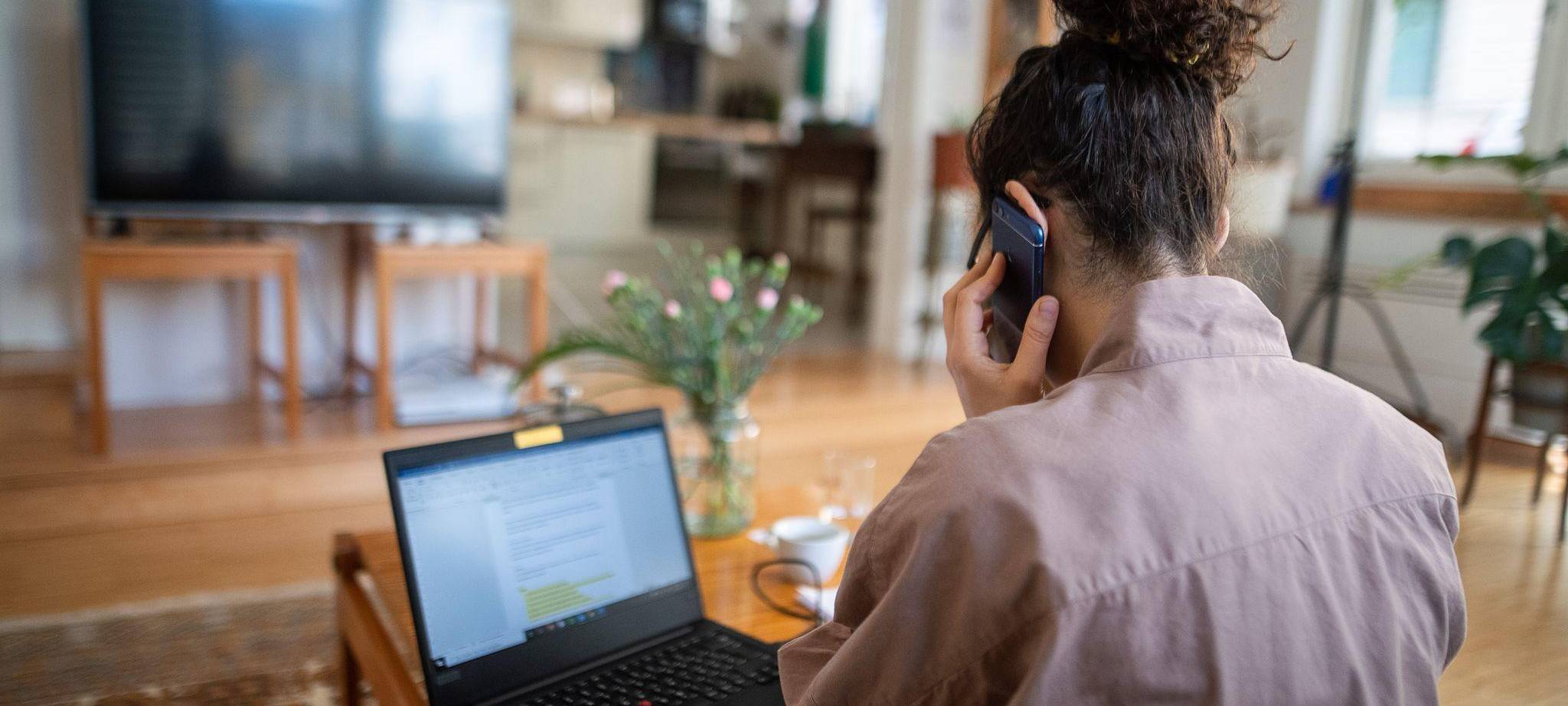 Eine Frau telefoniert vor einem geöffneten Laptop zu Hause